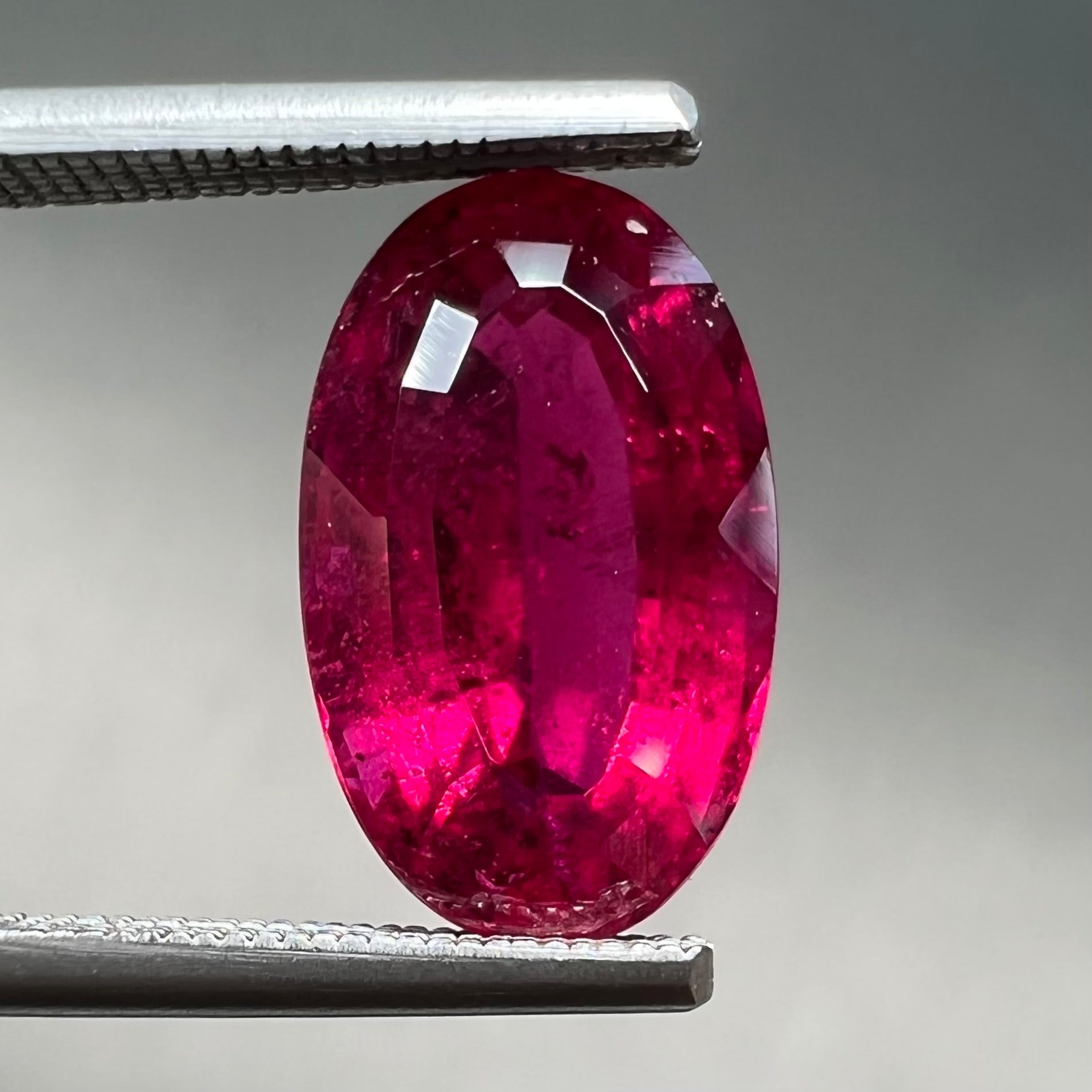 A loose, oval cut, purplish red rubellite tourmaline stone.