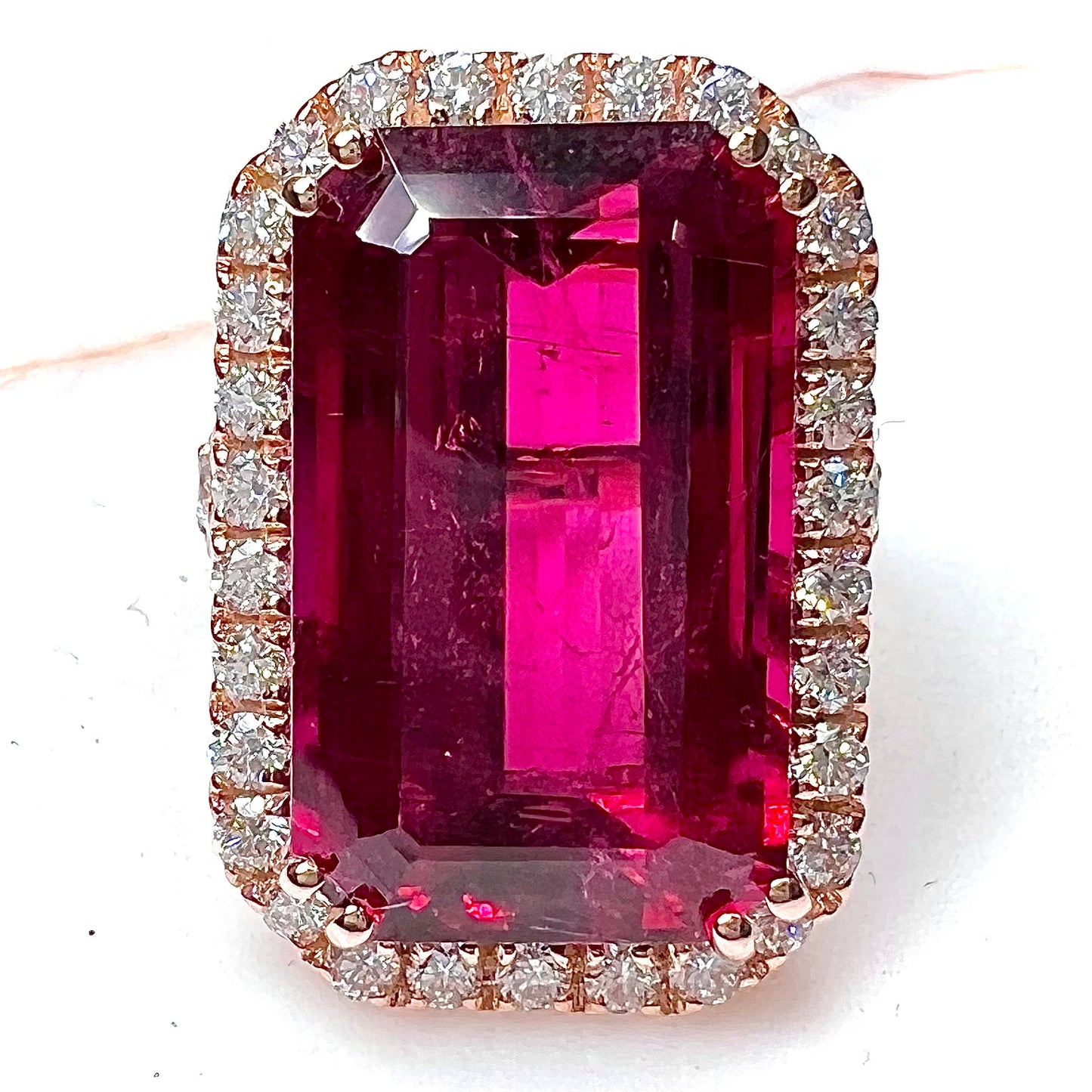 Red emerald cut rubellite tourmaline gemstone set with near flawless round cut diamonds in rose gold.