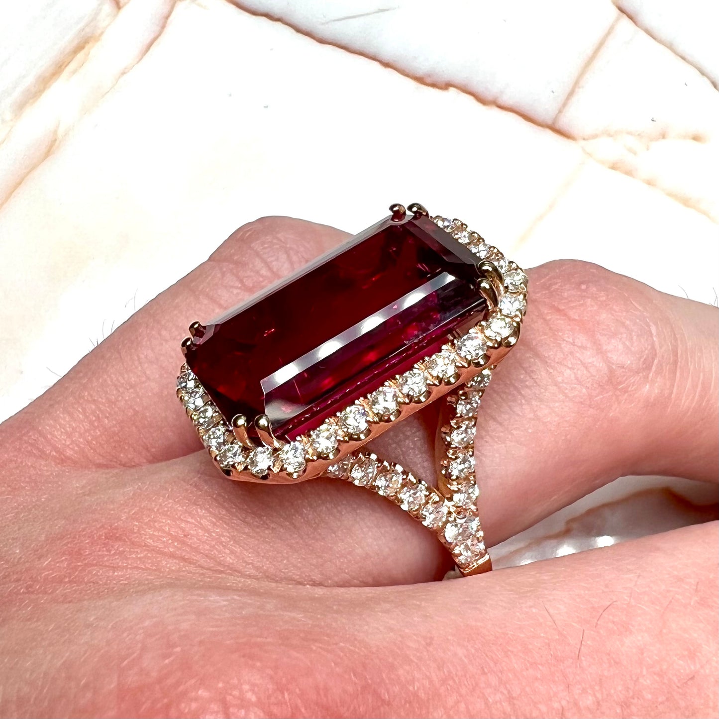 Red emerald cut rubellite tourmaline gemstone set with near flawless round cut diamonds in rose gold.