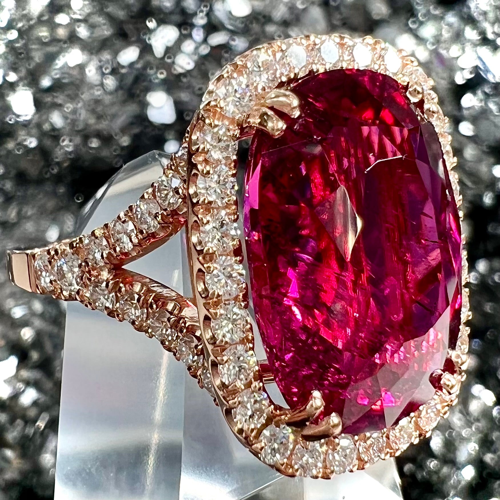 A rose gold, split shank engagement ring set with a cushion cut rubellite tourmaline in a diamond halo.