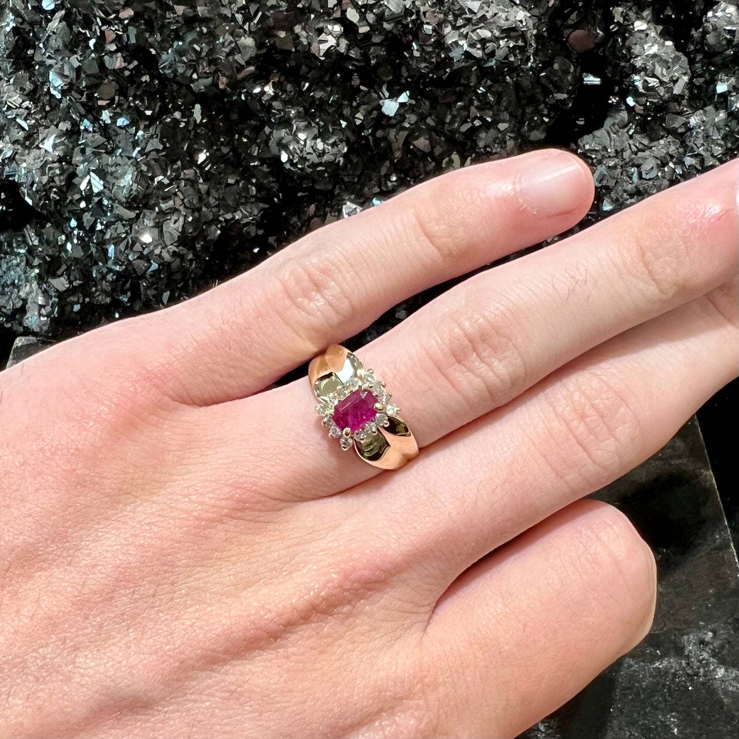 A yellow gold ring set with an emerald cut red ruby surrounded by a halo of round diamonds.