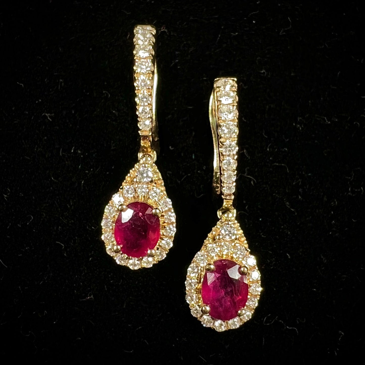 A pair of ruby and diamod halo dangle earrings cast in 14k yellow gold.