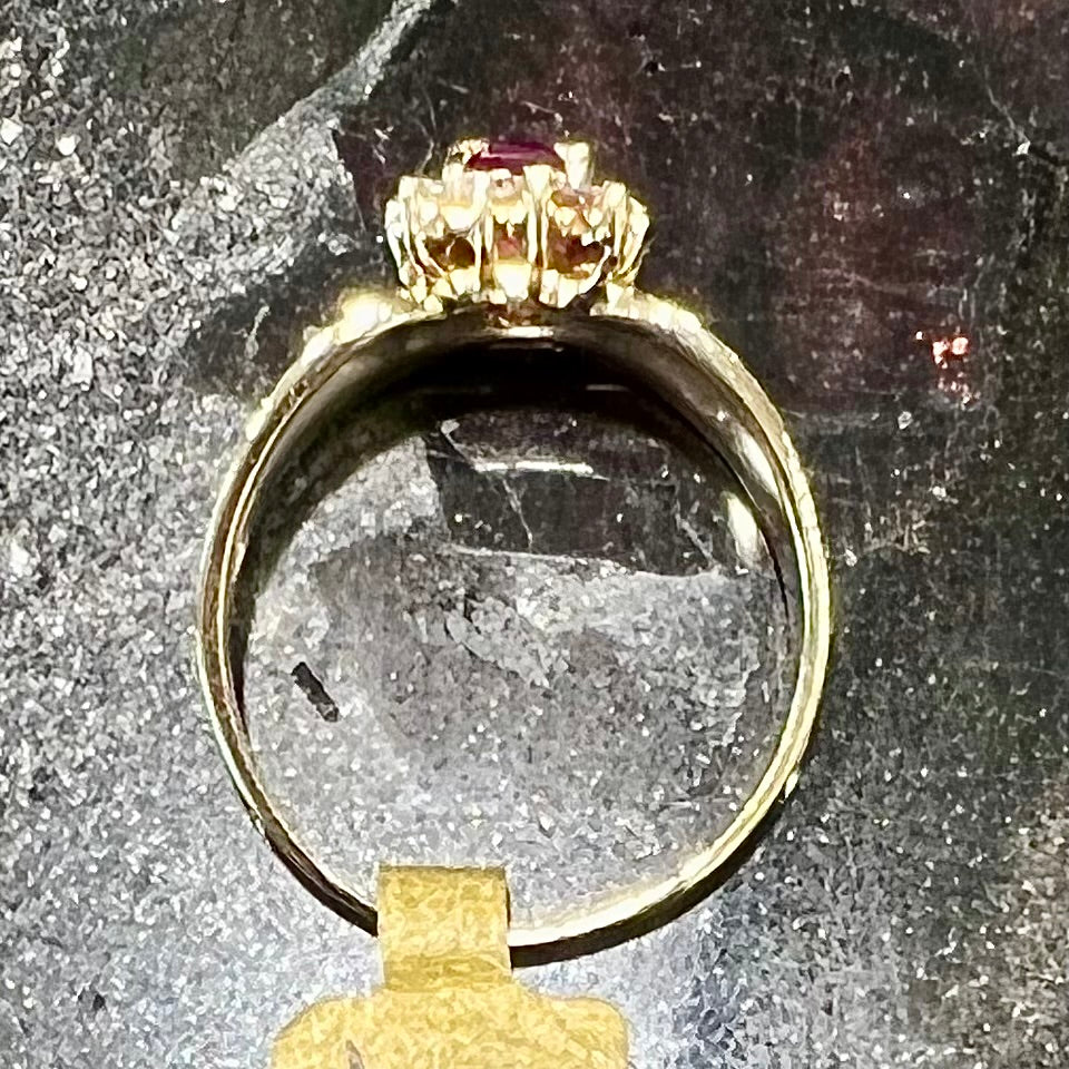 A yellow gold ring set with an emerald cut red ruby surrounded by a halo of round diamonds.