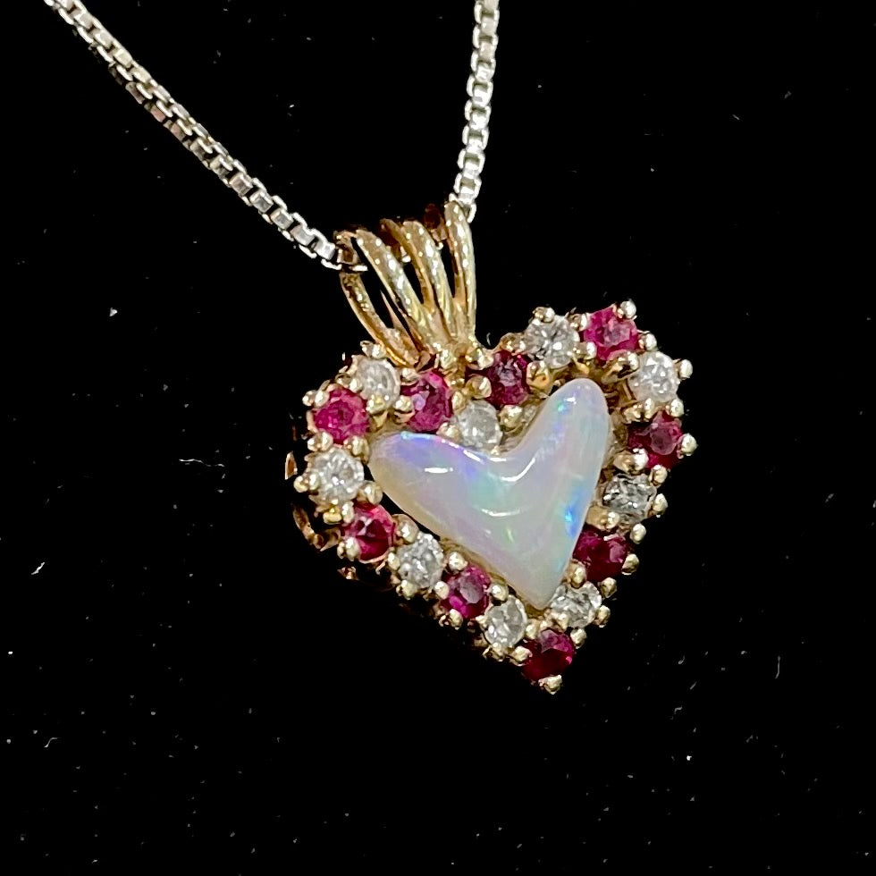 A yellow gold pendant set with a heart cut white opal in a halo of alternating round rubies and diamonds.