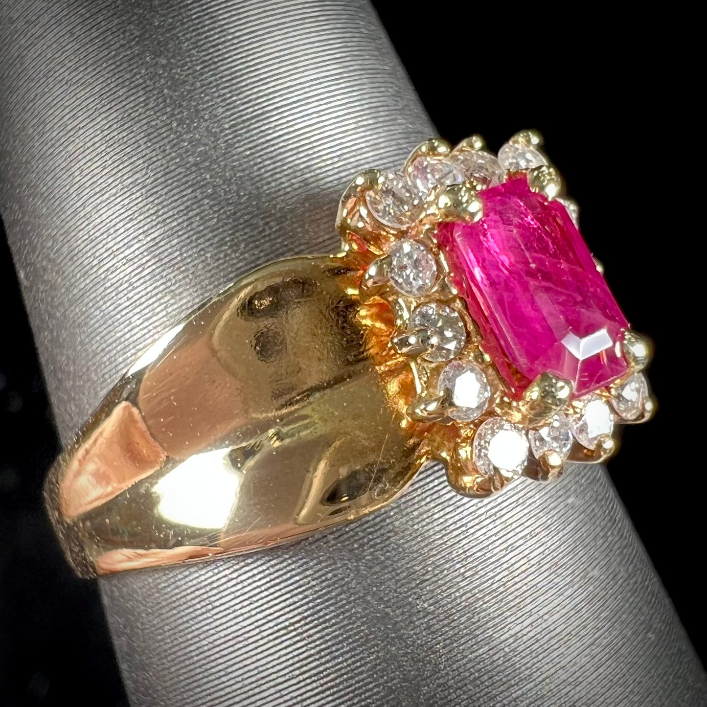 A yellow gold ring set with an emerald cut red ruby surrounded by a halo of round diamonds.