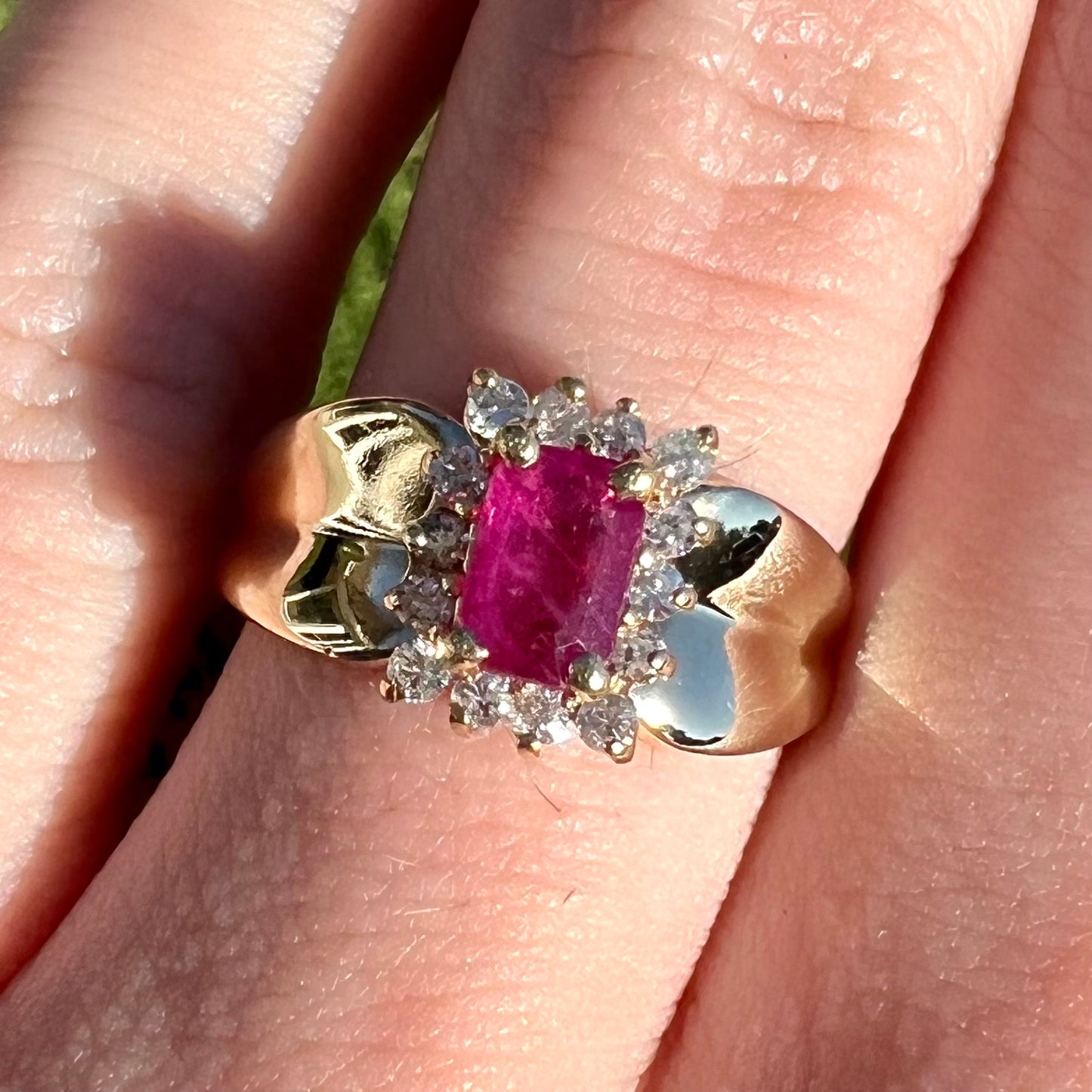 A yellow gold ring set with an emerald cut red ruby surrounded by a halo of round diamonds.