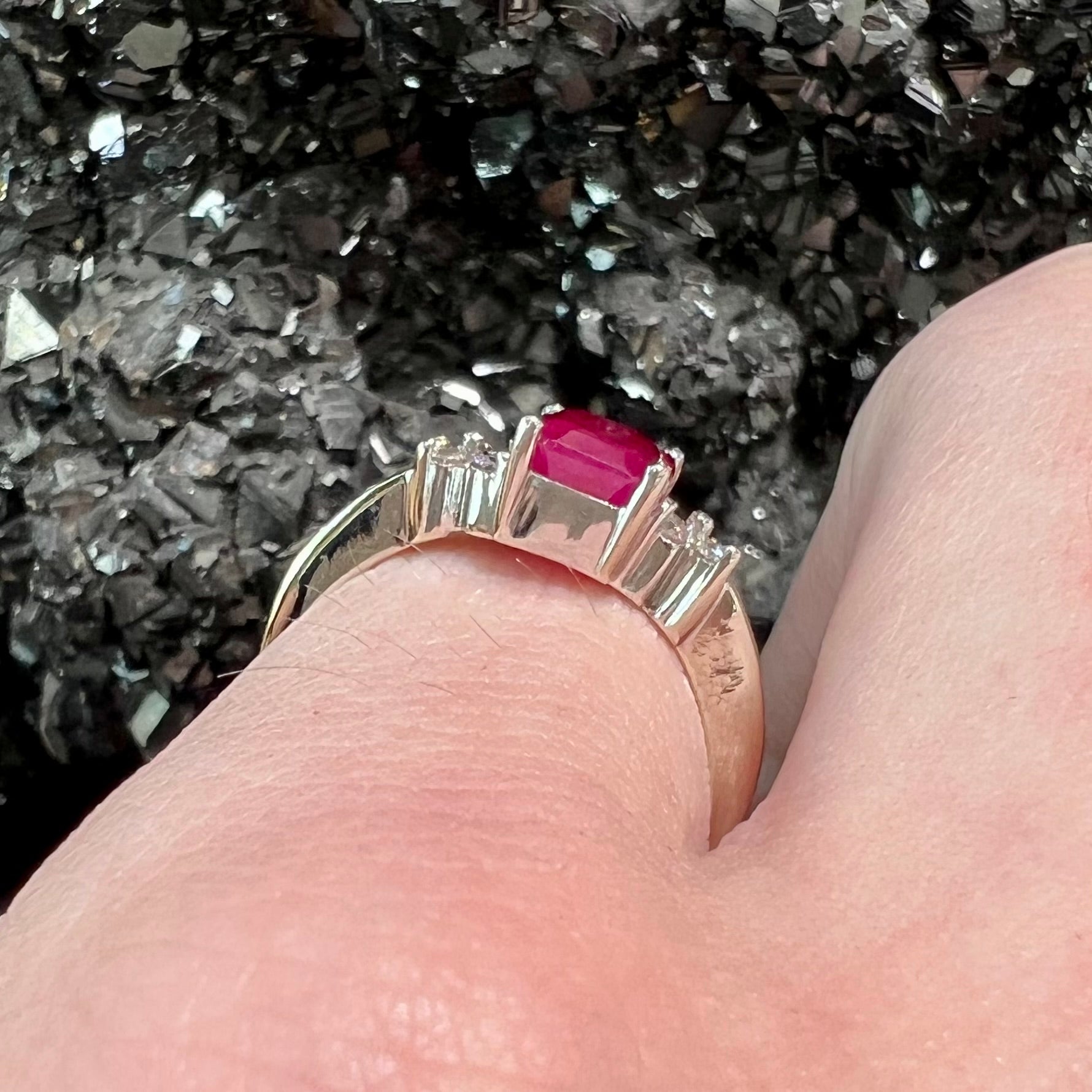 A white gold ring with an emerald cut red synthetic ruby set between four round cut diamonds on each side.