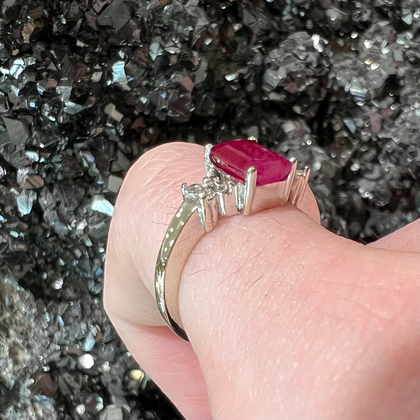 A white gold ring with an emerald cut red synthetic ruby set between four round cut diamonds on each side.