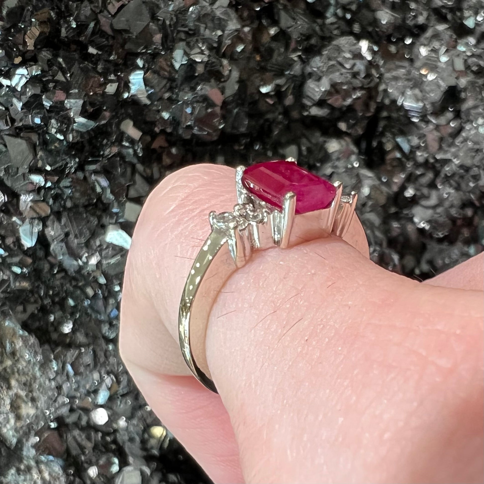 A white gold ring with an emerald cut red synthetic ruby set between four round cut diamonds on each side.