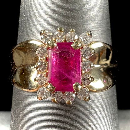 A yellow gold ring set with an emerald cut red ruby surrounded by a halo of round diamonds.