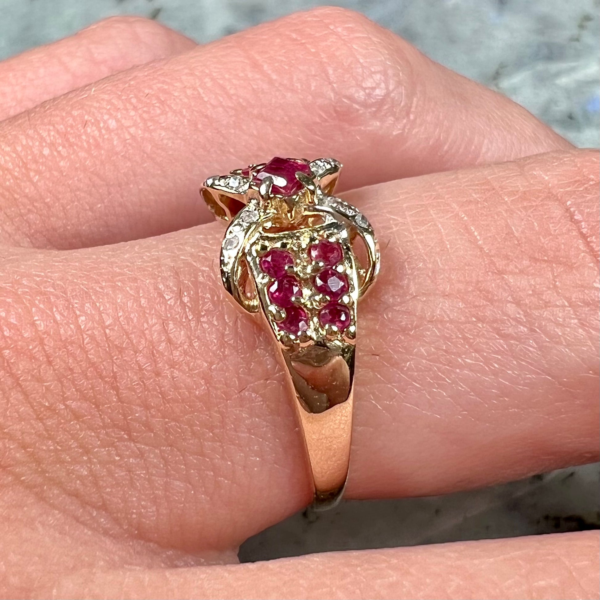 A yellow gold princess cut ruby ring set with round ruby and diamond accents.