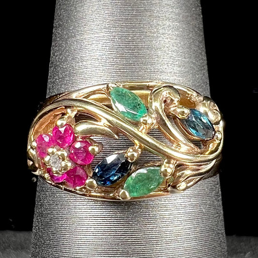 A yellow gold ladies' ring featuring the motif of a flower with leaves set with emeralds, rubies, sapphires, and a  diamond.