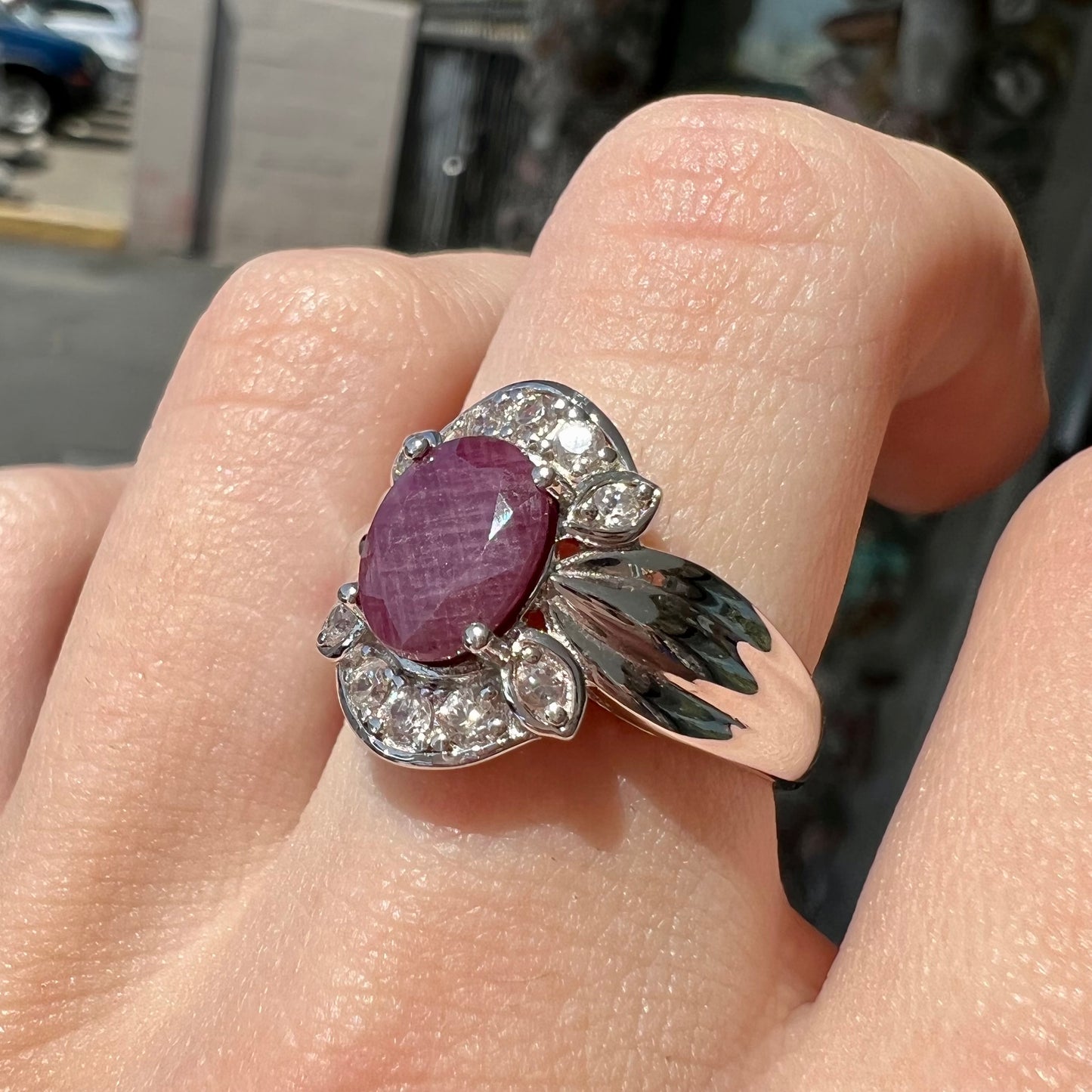 A natural, faceted oval cut ruby ring cast in sterling silver and set with cubic zirconia accents.