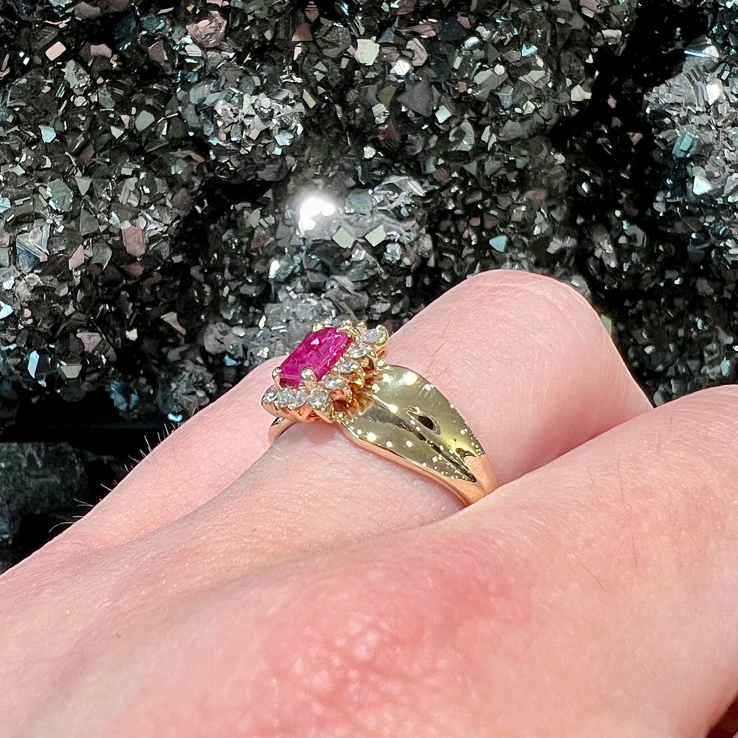 A yellow gold ring set with an emerald cut red ruby surrounded by a halo of round diamonds.