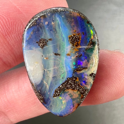 A loose, pear shaped Australian boulder opal.  The pattern on the opal resembles the face of a very sad man.