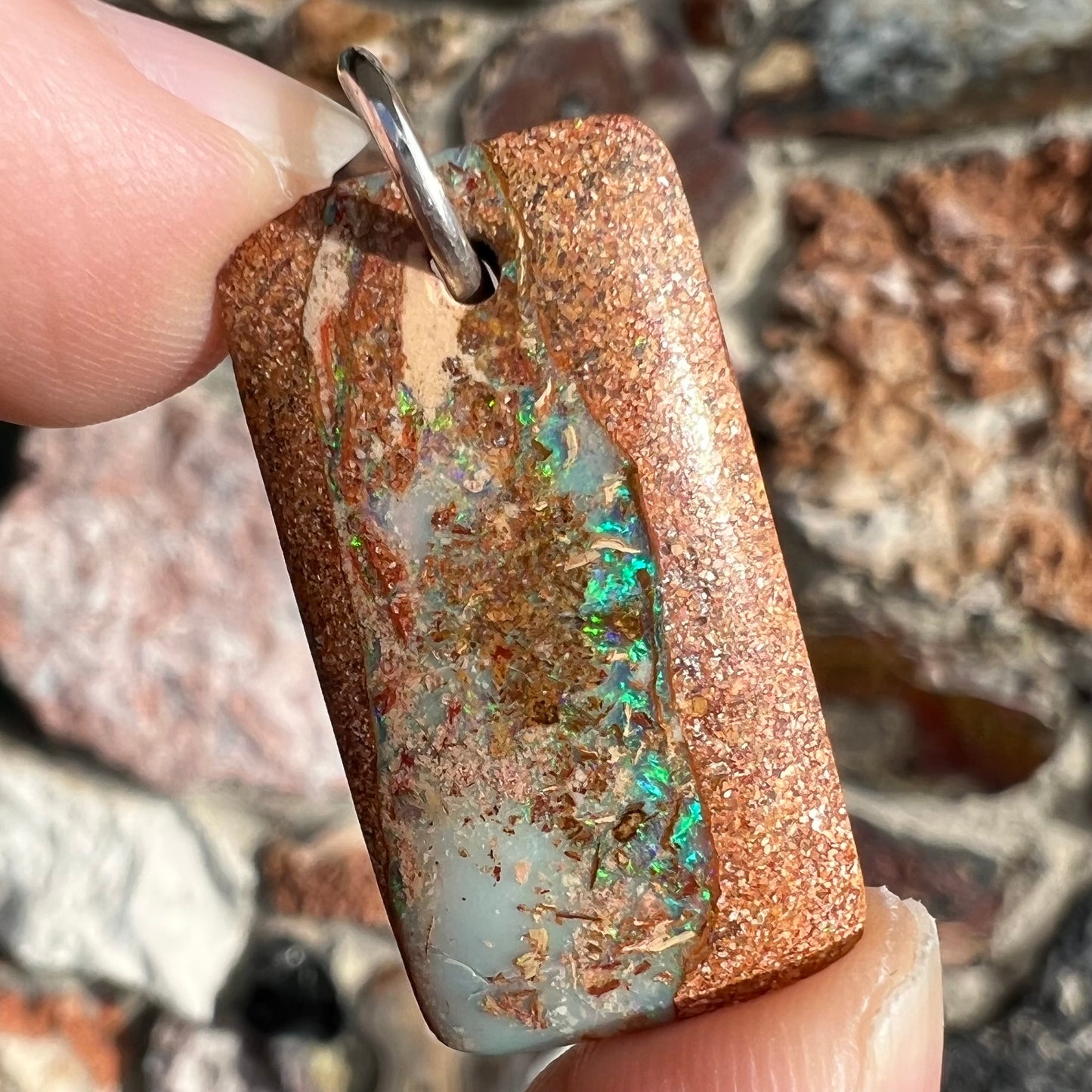 A drilled boulder opal stone with a sterling silver ring through the hole to be worn as a pendant.