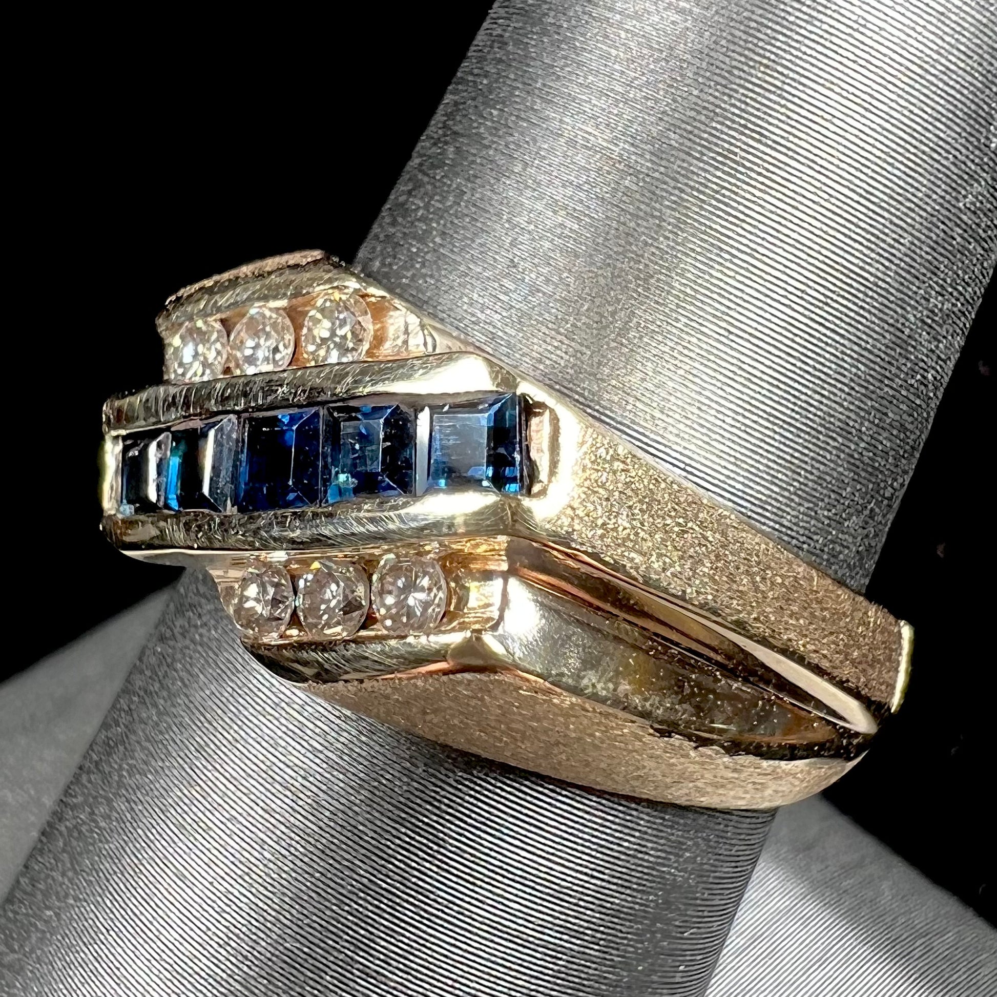 A men's yellow gold ring channel set with princess cut blue sapphires and diamonds.