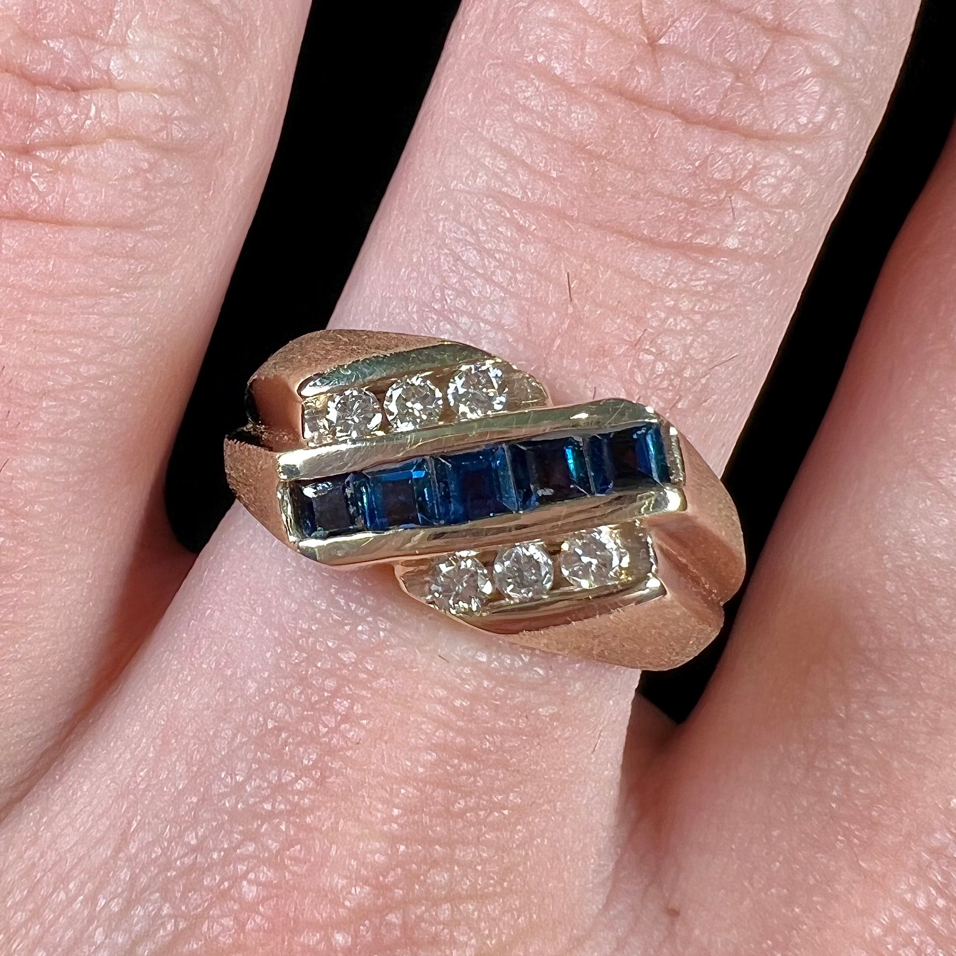 A men's yellow gold ring channel set with princess cut blue sapphires and diamonds.