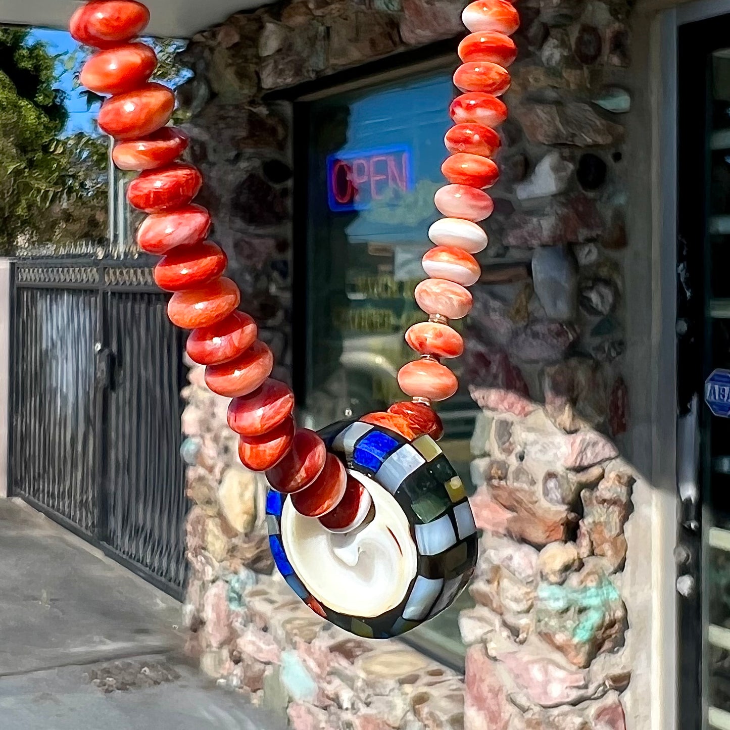 A handmade seashell pendant inlaid with spiny oyster, mother of pearl, and lapis lazuli on a spiny oyster bead necklace by Charlene Reano.