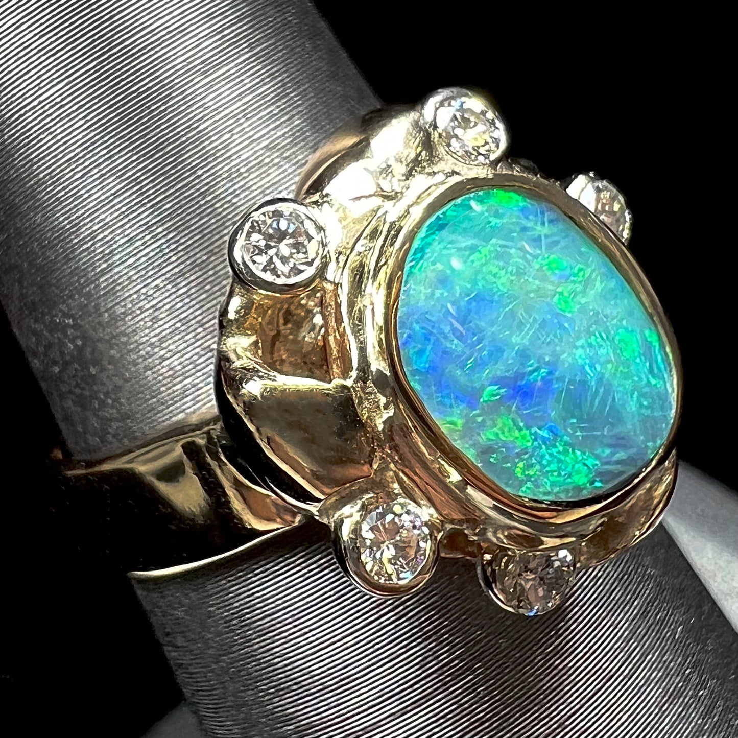 A ladies' yellow gold oval cut natural black opal ring set with five round accent diamonds.