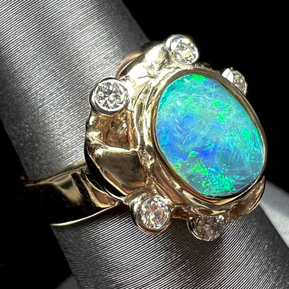 A ladies' yellow gold oval cut natural black opal ring set with five round accent diamonds.