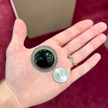 A sterling silver pendant/brooch bezel set with a round cabochon cut black sheen obsidian stone.