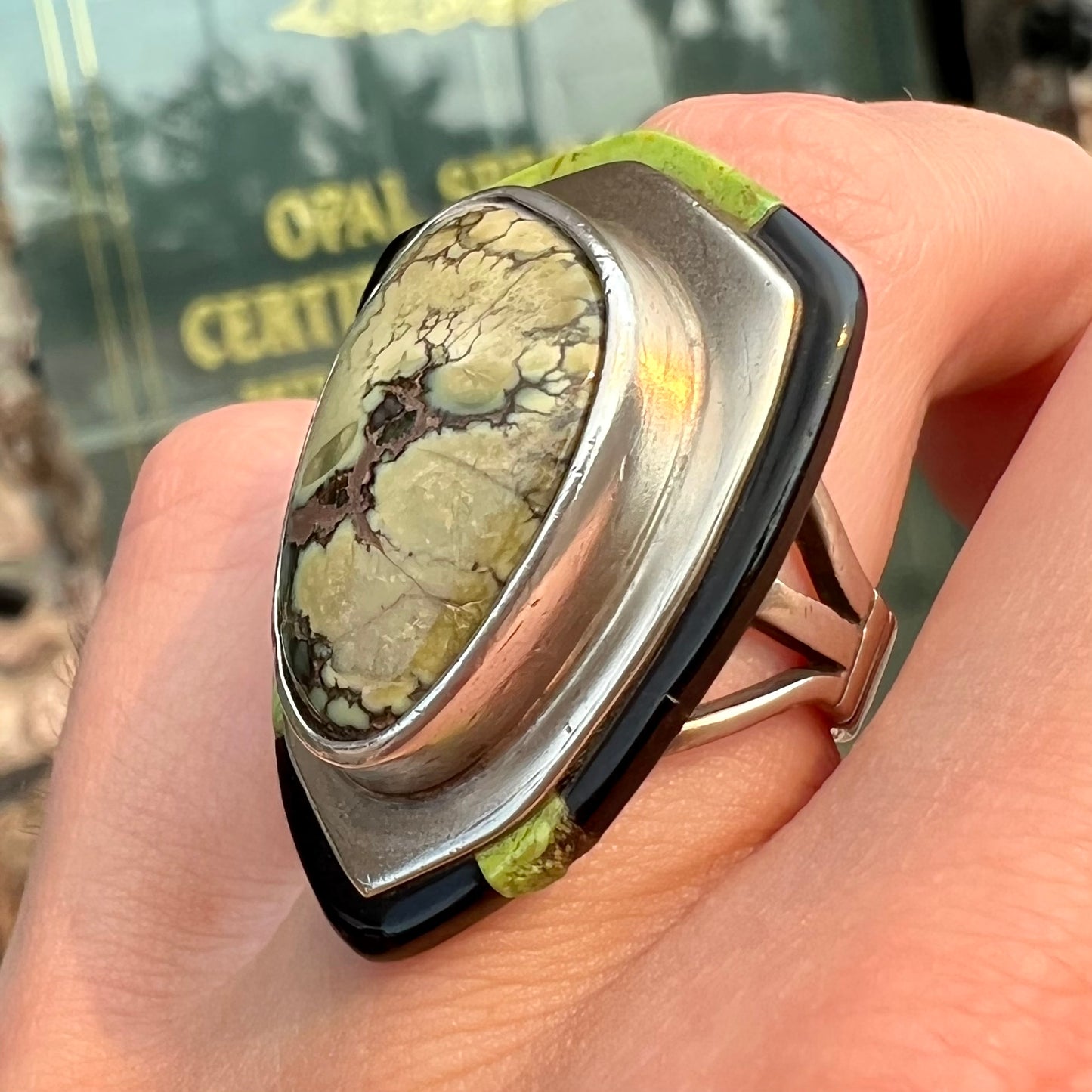 A shield shaped silver ring bezel set with a green gaspeite stone with stone inlaid edges, handmade by artist Benny Armijo.