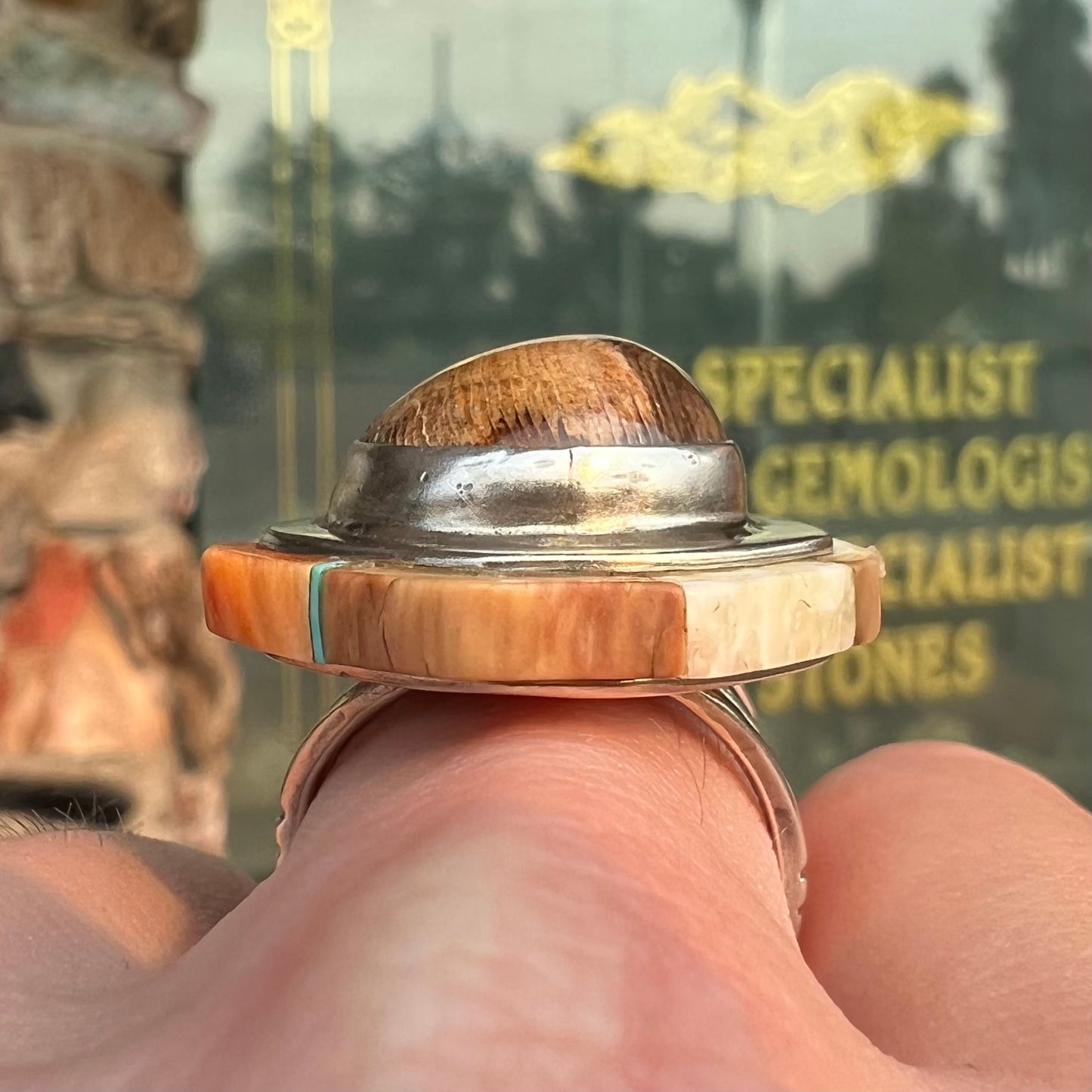 A silver ring handmade from a bezel set petrified wood stone, surrounded by quartz, carnelian, and bone inlay.