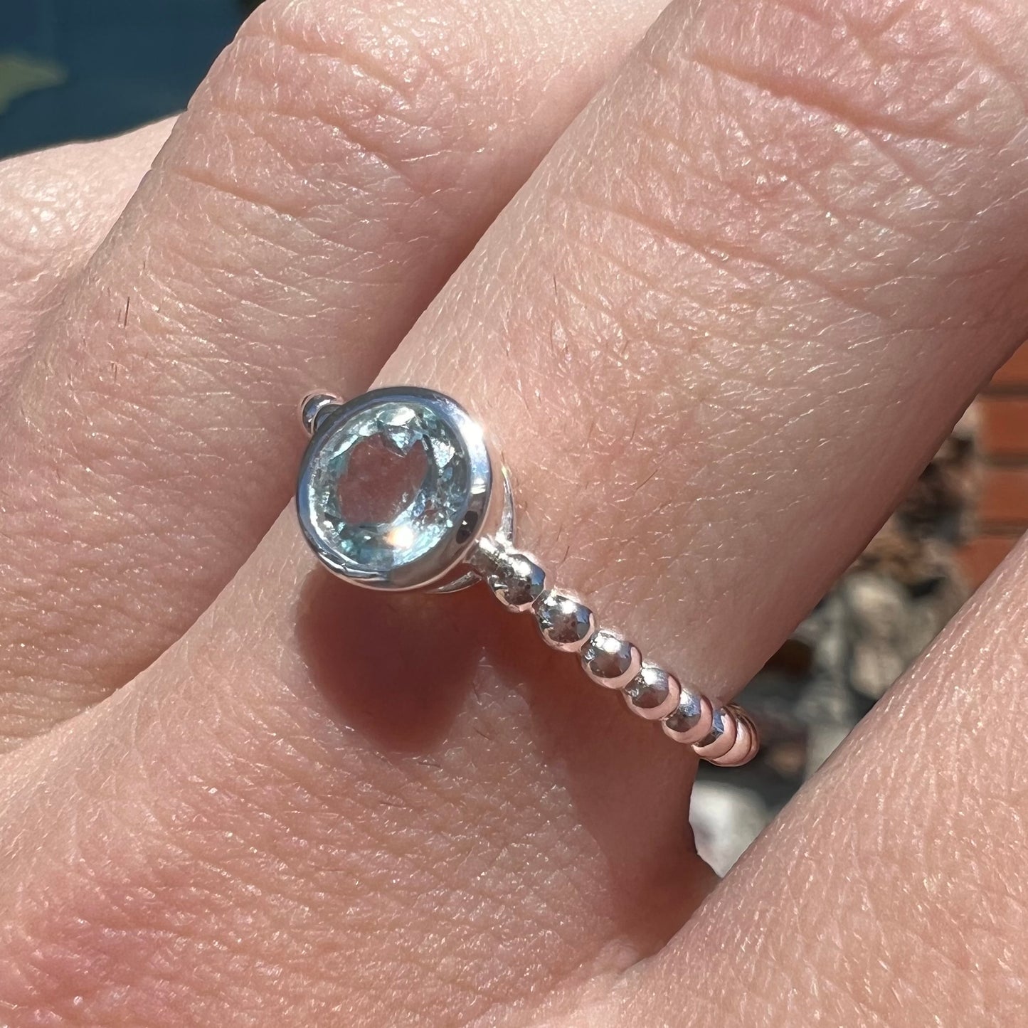 A silver, bezel set, round cut sky blue topaz solitaire ring.  The band is made of connected silver balls.