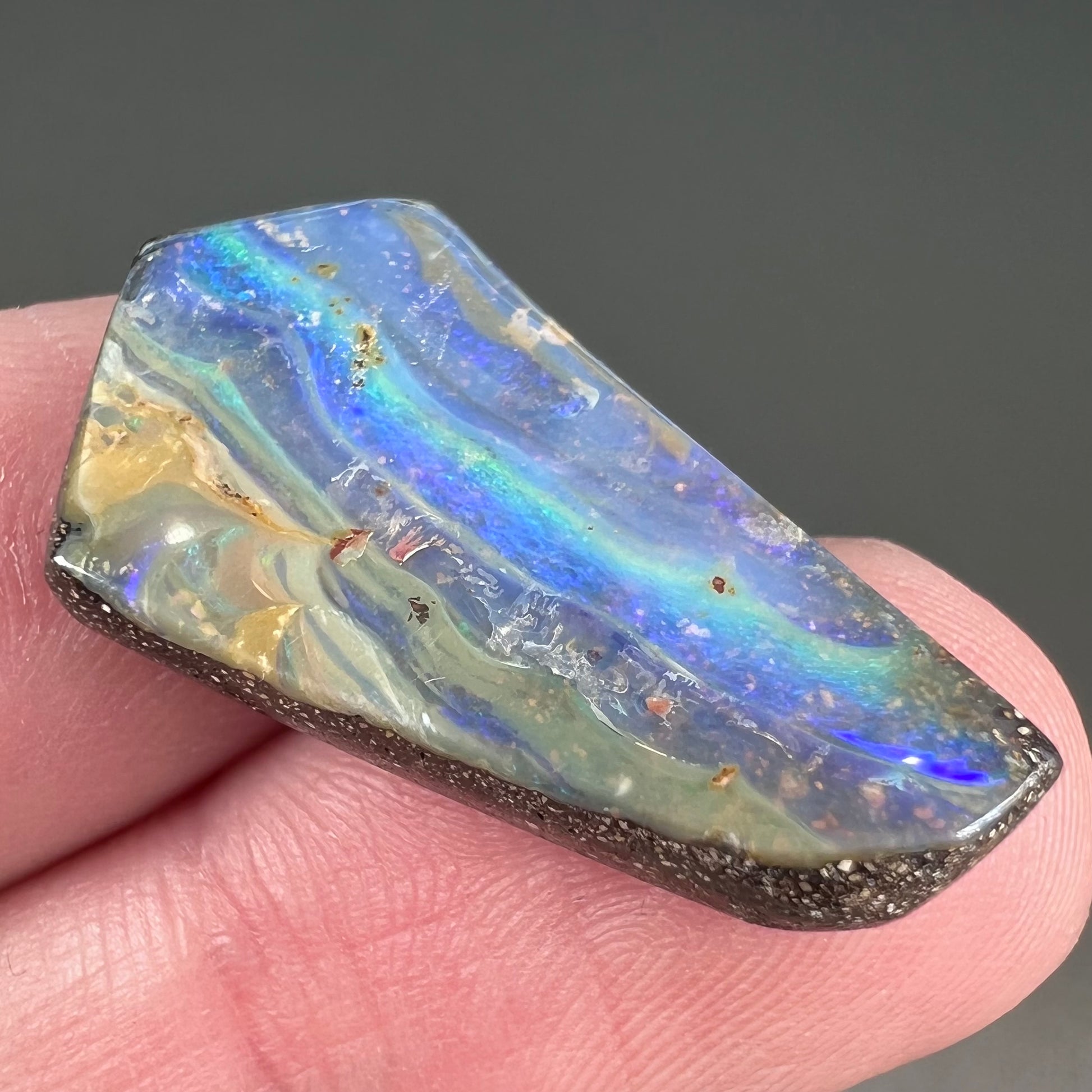 A loose, polished, freeform cut boulder opal stone from Queensland, Australia.