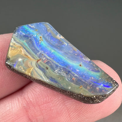 A loose, polished, freeform cut boulder opal stone from Queensland, Australia.
