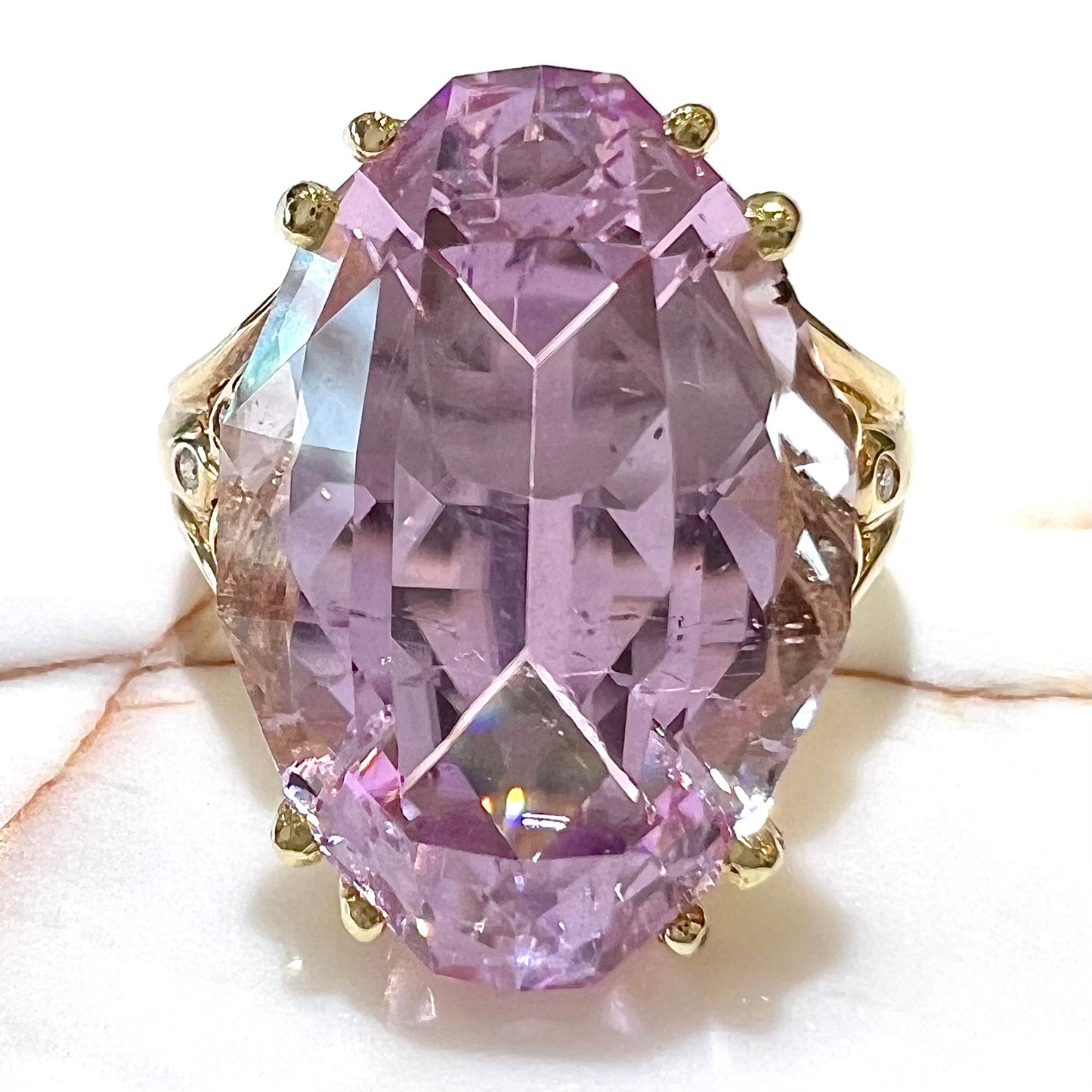 A large, pink kunzite is prong set into a 14kt yellow gold basket-style ring mounting with three diamonds flush set into the design on each side.