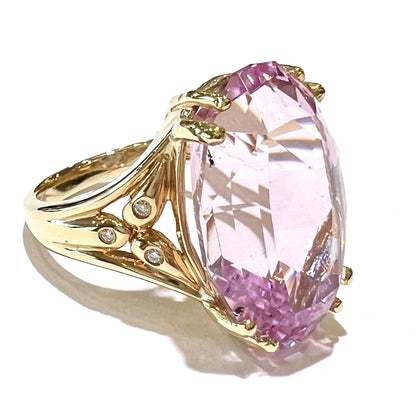 A large, pink kunzite is prong set into a 14kt yellow gold basket-style ring mounting with three diamonds flush set into the design on each side.