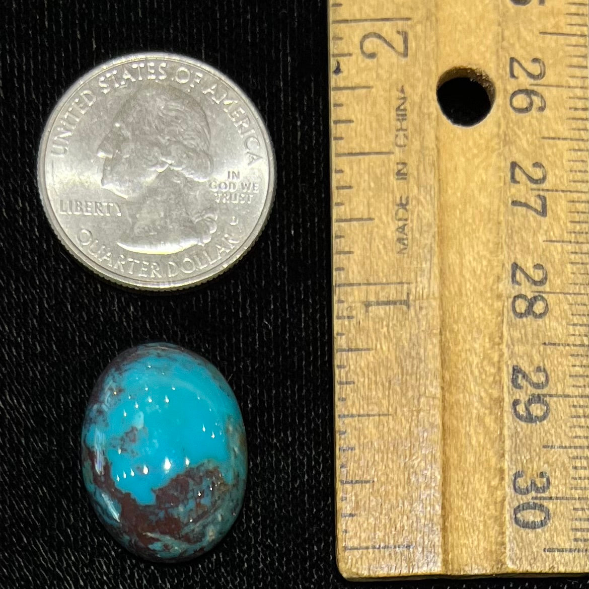 An oval cabochon cut blue turquoise stone with red cuprite inclusions from Royston District, Nevada.