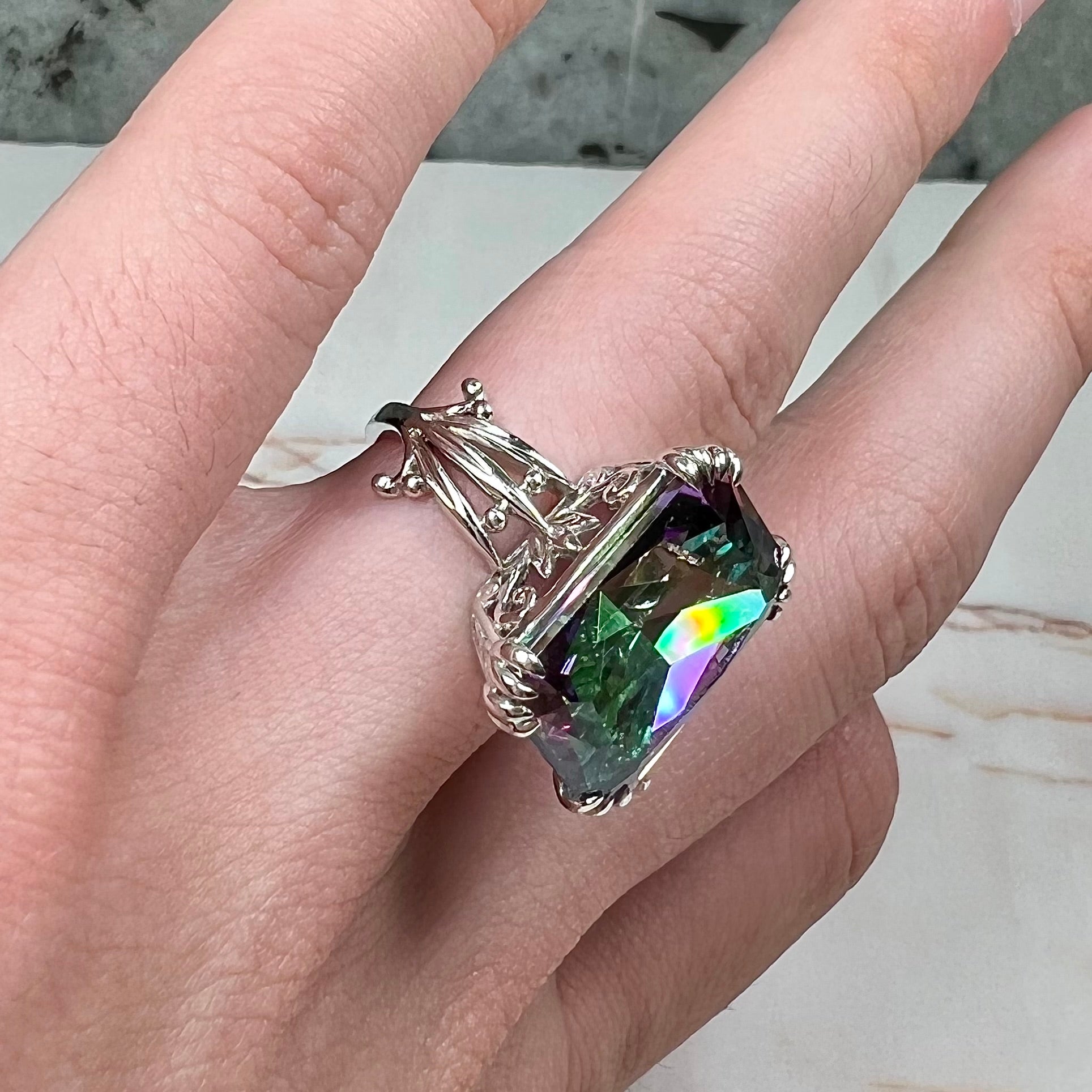 Emerald cut mystic topaz prong set in a decorative sterling silver ring.