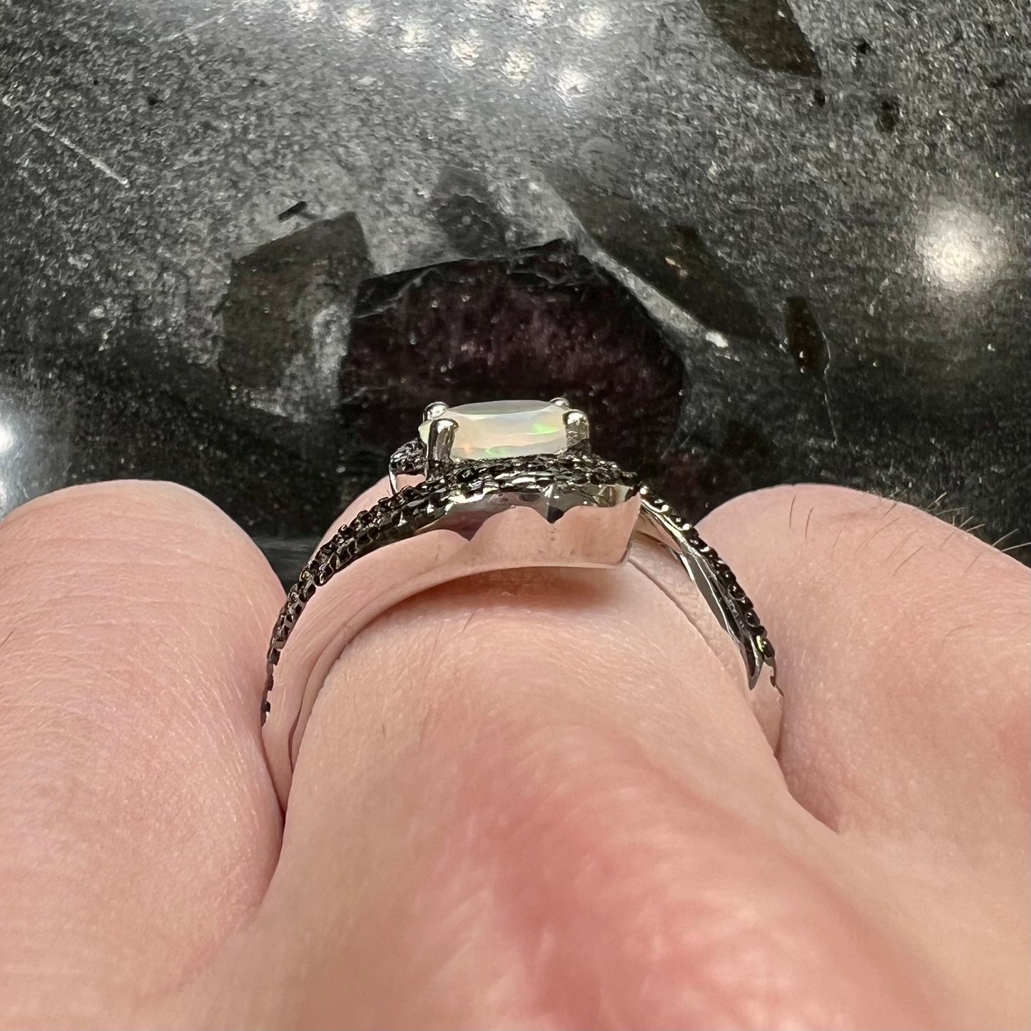 A sterling silver ring set with round black spinel stones and an oval cut, faceted Ethiopian opal.
