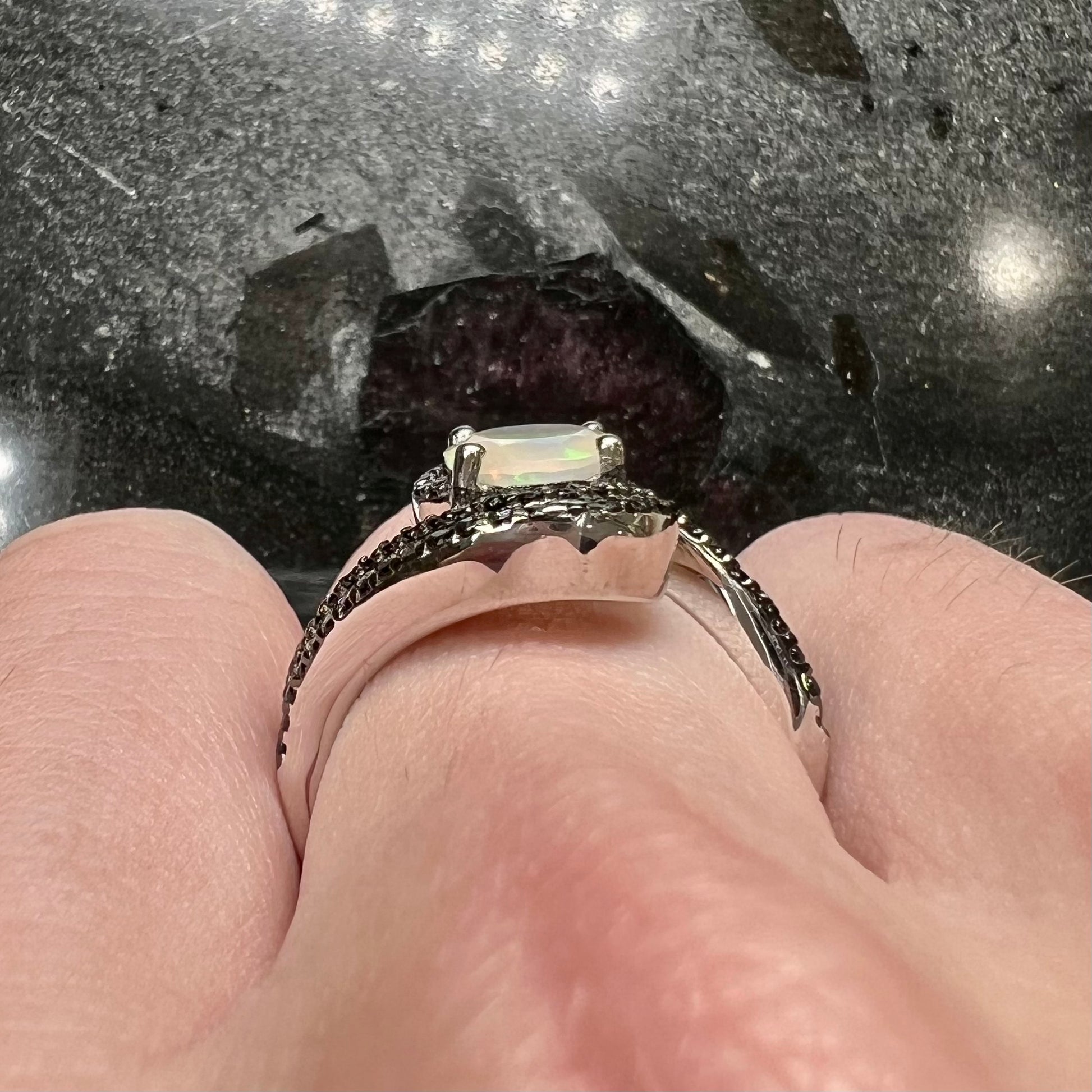 A sterling silver ring set with round black spinel stones and an oval cut, faceted Ethiopian opal.