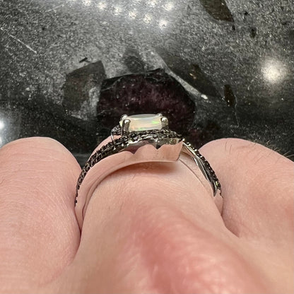 A sterling silver ring set with round black spinel stones and an oval cut, faceted Ethiopian opal.
