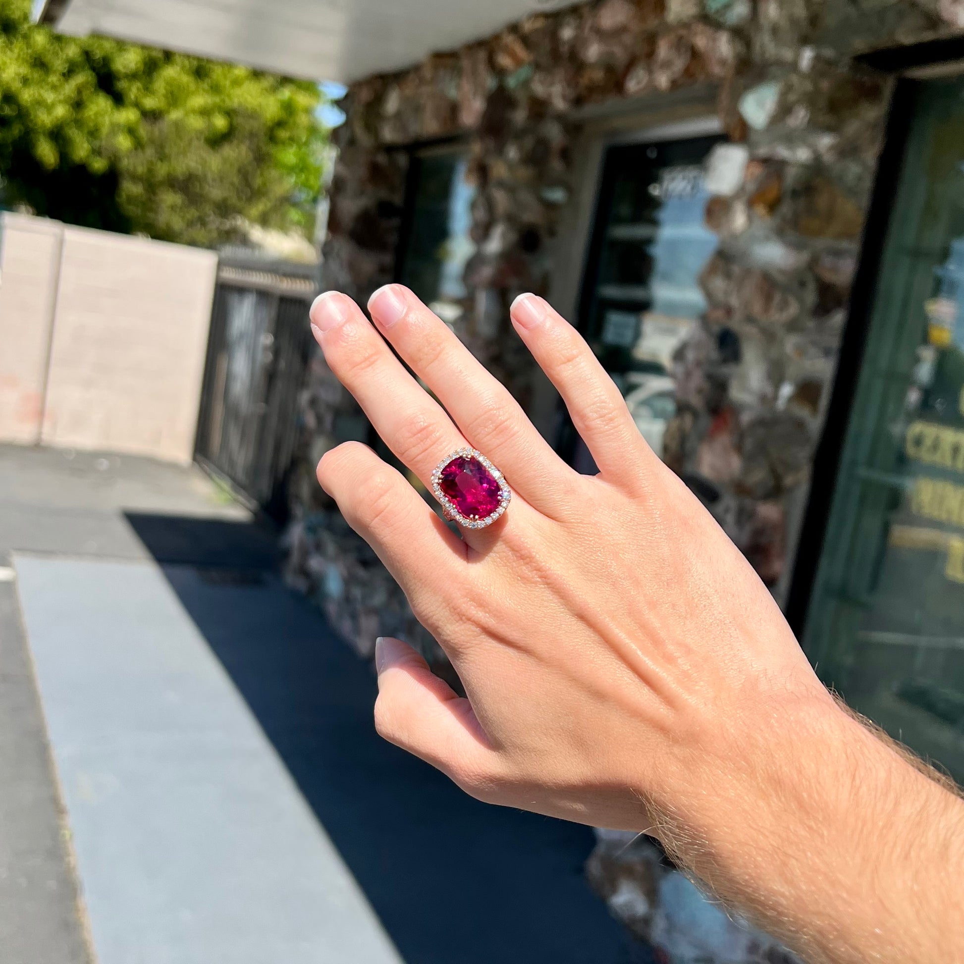 A rose gold, split shank engagement ring set with a cushion cut rubellite tourmaline in a diamond halo.
