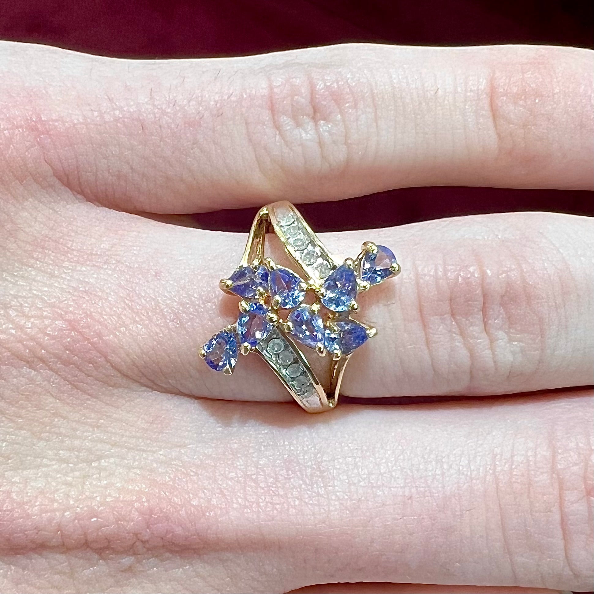 A pear shape tanzanite cluster ring channel set with diamonds in yellow gold.