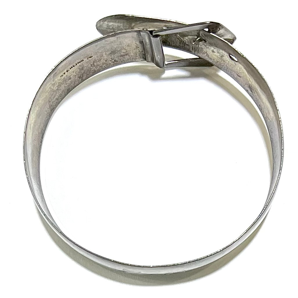 A photo showing the profile of a sterling silver antique Art Nouveau buckle bracelet.  The bracelet is engraved and etched with a floral pattern design.  The word "STERLING" is seen.