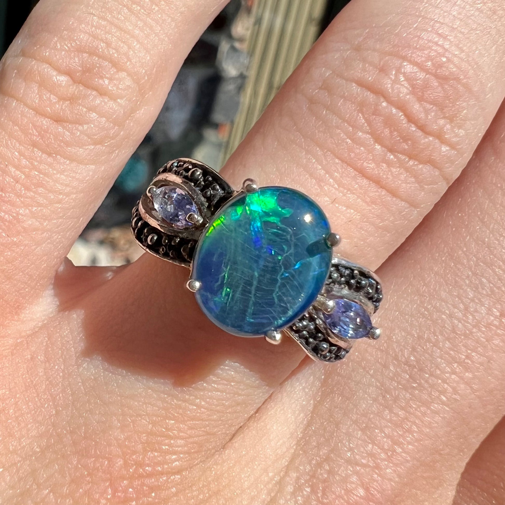 A sterling silver ring set with a black opal triplet, two marquise cut tanzanites, and round black spinel accent stones.