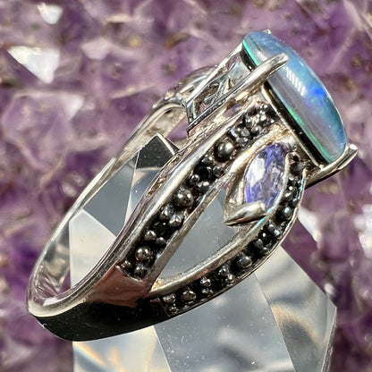 A sterling silver ring set with a black opal triplet, two marquise cut tanzanites, and round black spinel accent stones.