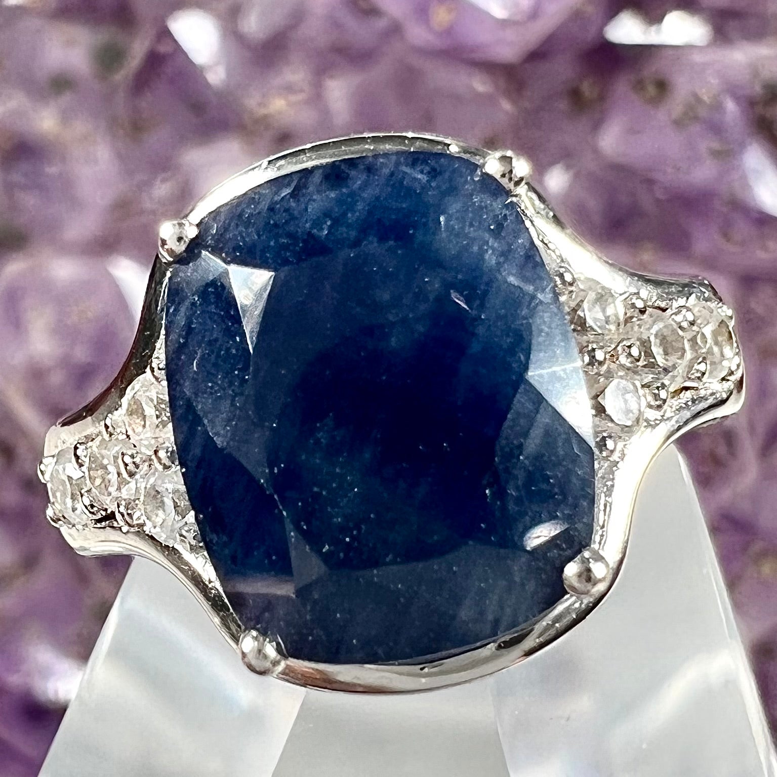 A sterling silver ring set with a cushion cut blue sapphire center stone and round cut white sapphire accents.