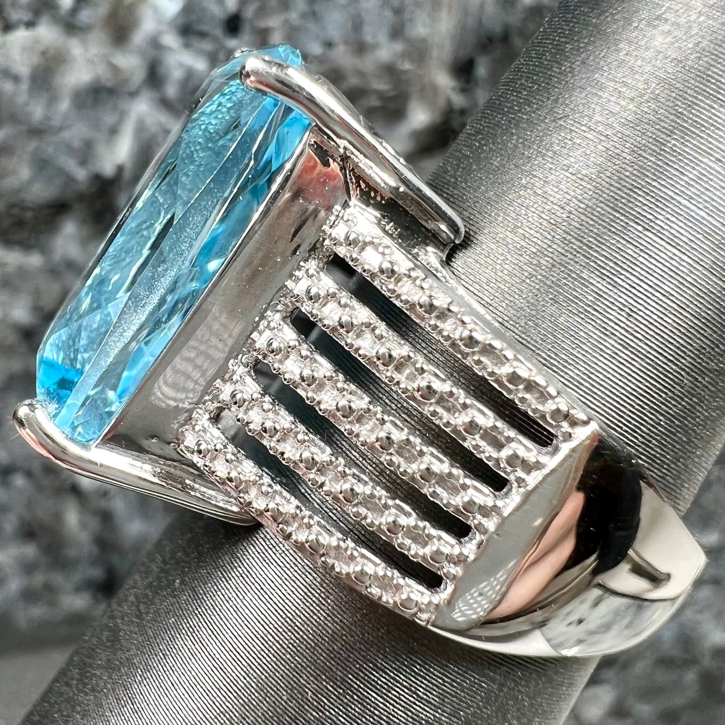 A sterling silver ring prong set with a large, cushion cut sky blue topaz stone.  The shank has been textured to mimic accent stones.