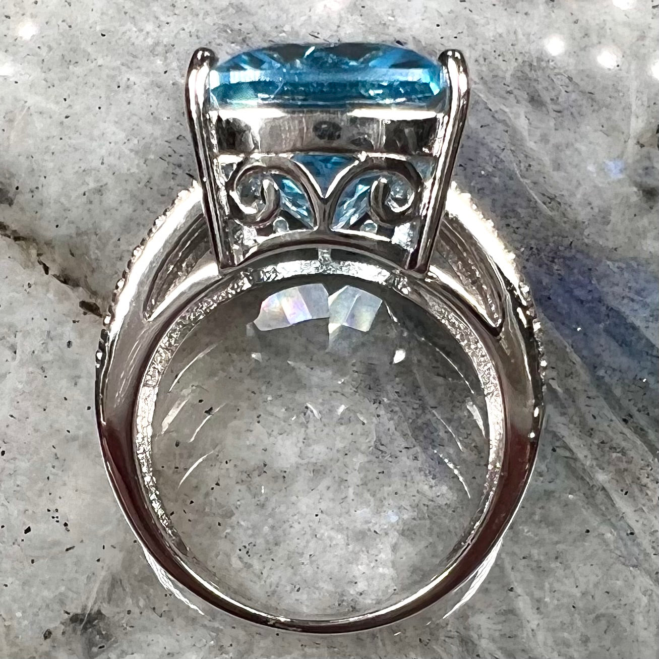 A sterling silver ring prong set with a large, cushion cut sky blue topaz stone.  The shank has been textured to mimic accent stones.