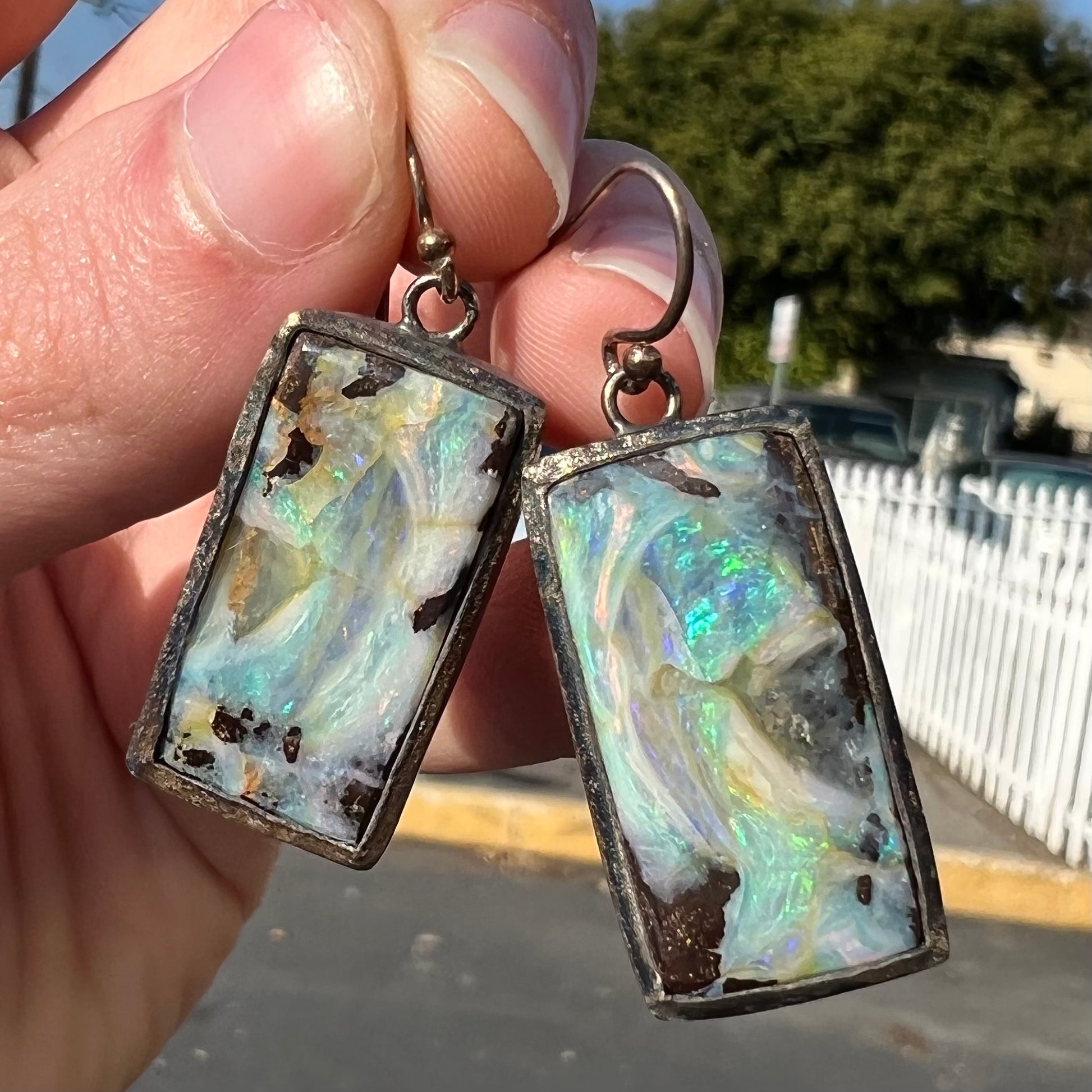 A pair of handmade sterling silver boulder opal earrings.  The earrings dangle from French wire hooks.
