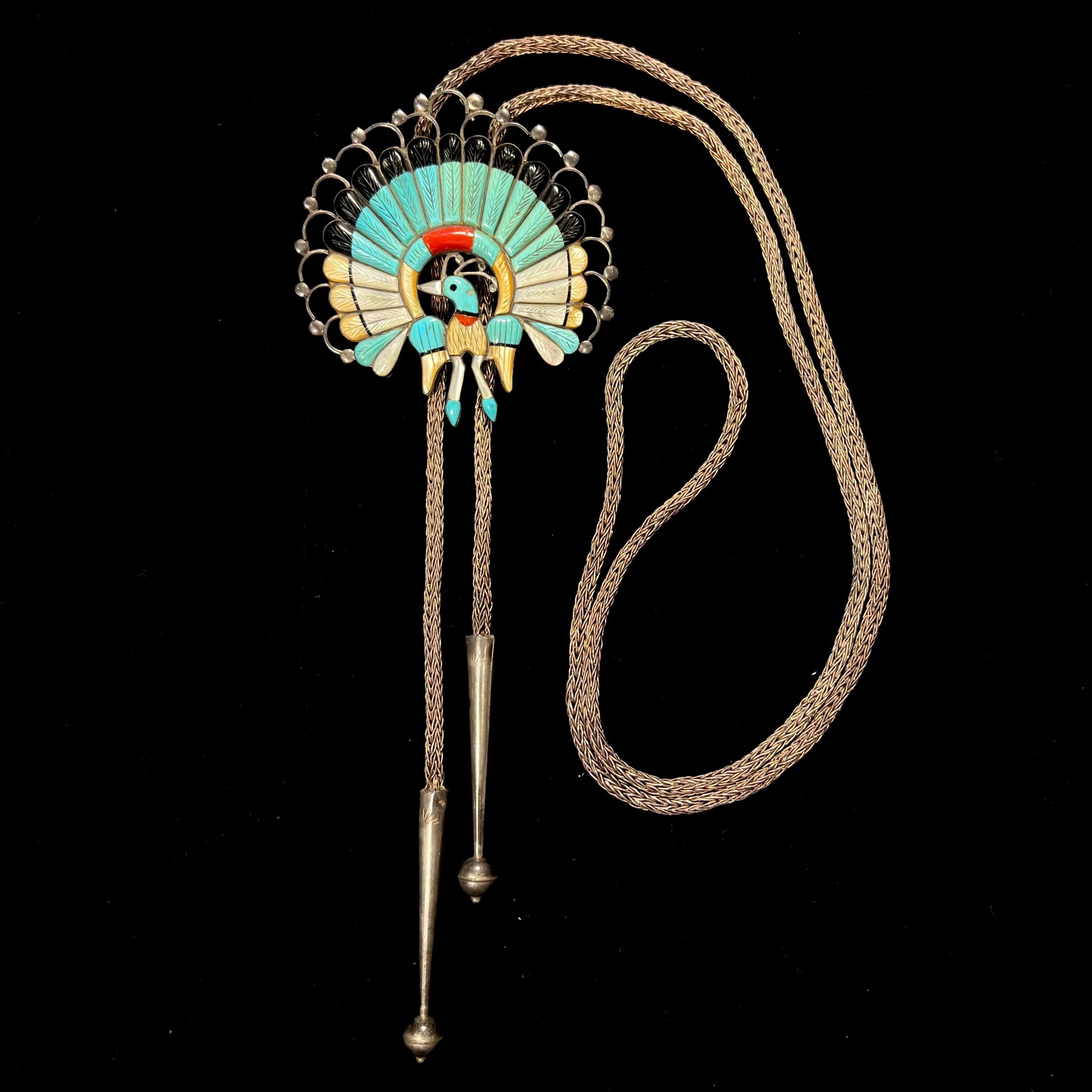 A handmade Zuni style stone inlay peacock bolo tie set with onyx, coral, turquoise, and gold lipped pearl on a silver bolo chain.