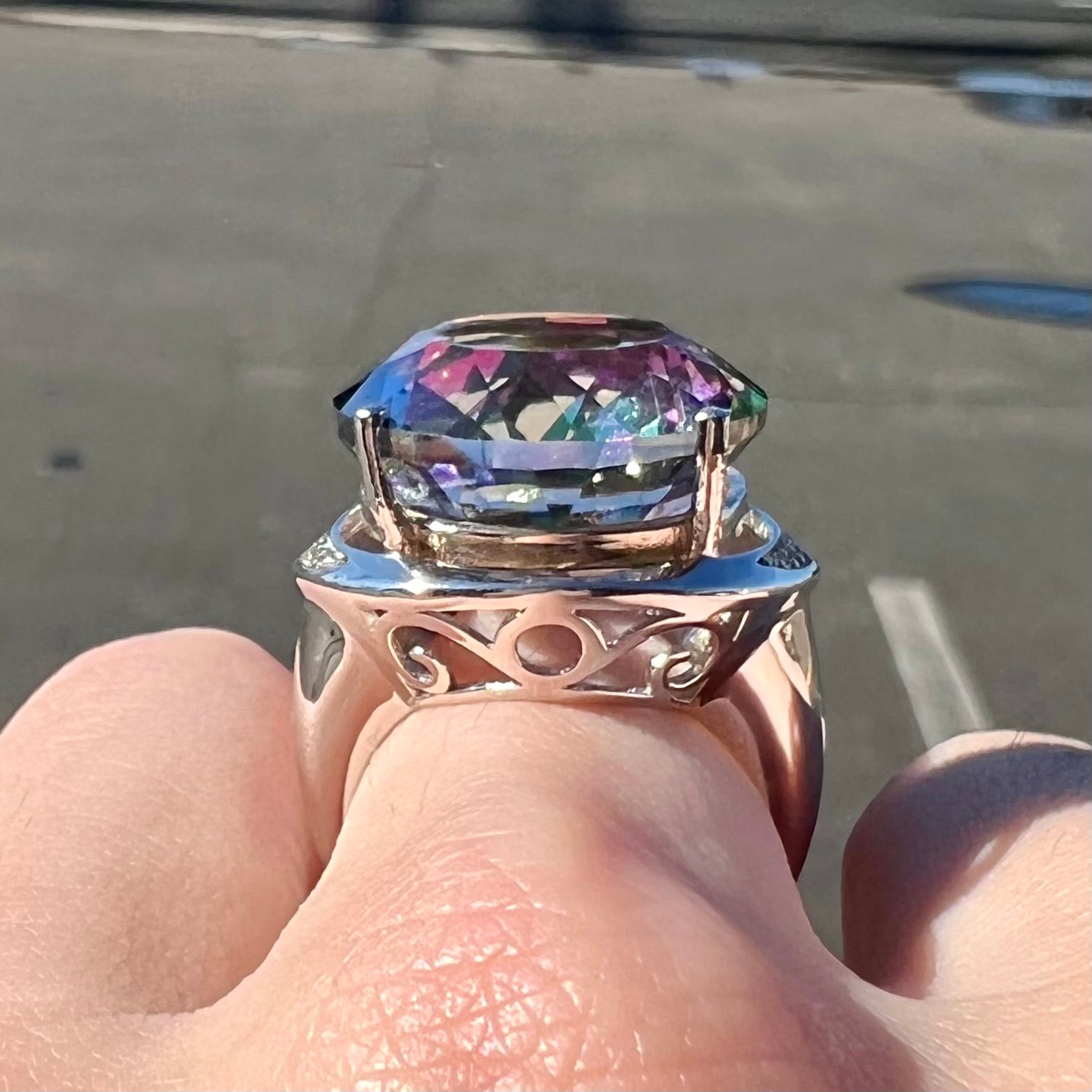 A large, round cut pink and green mystic topaz set in a sterling silver ring with white topaz accent stones.
