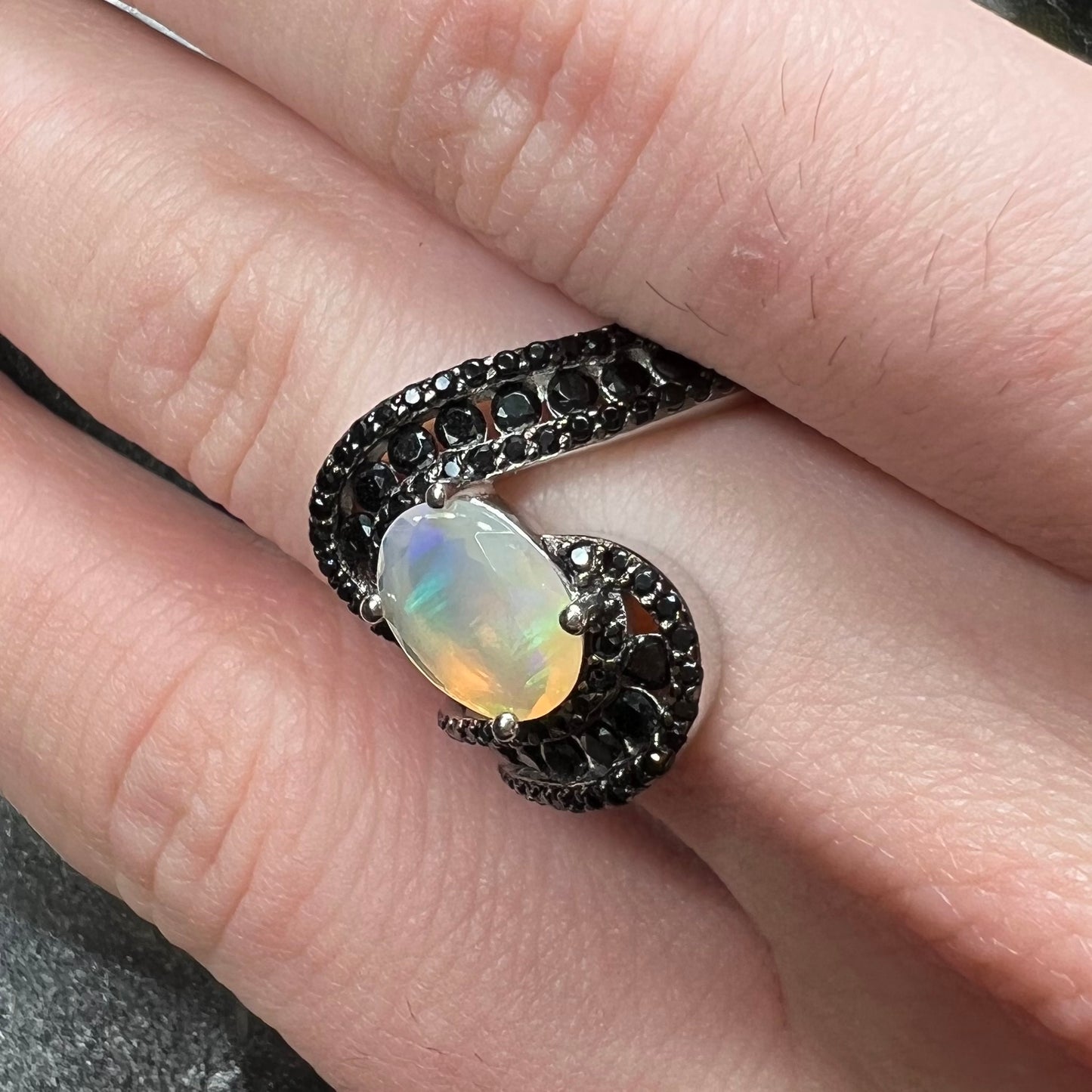 A sterling silver ring set with round black spinel stones and an oval cut, faceted Ethiopian opal.